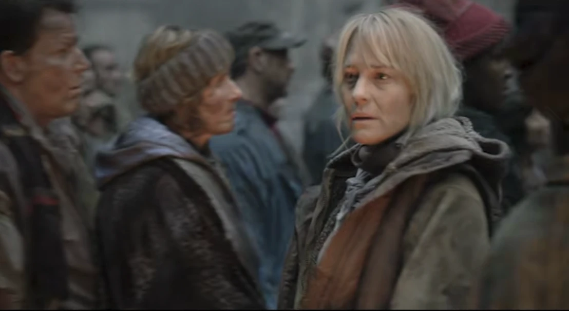 Robin Wright in a worn coat, looking worried in a crowd of tired, grey-clothed people.
